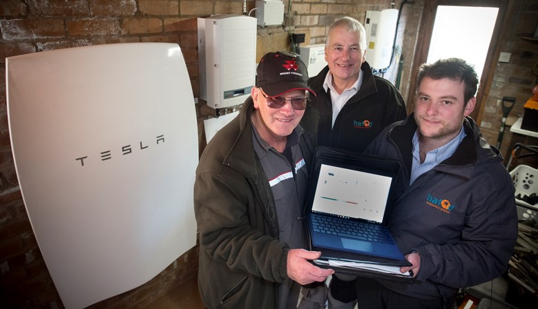 HAFOD RENEWABLES.... retired agricultural contractor Philip Johnson pictured with his new Tesla home battery in his garage with Richard and David Jones of Hafod Renewables.