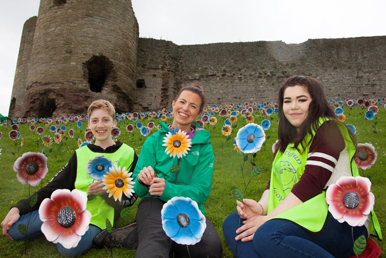 St Kentigern Hospice planted 1,000 metal flowers in the grounds of the castle as part of a public display and to form part of the Rhuddlan entry into Wales in Bloom Pictured bringing colour to t Rhuddlan Castle on a rainy day is fundraising manager Laura Parry with Ysgol Eirias pupils Ethan Hughes and Amber Lea Powell.
