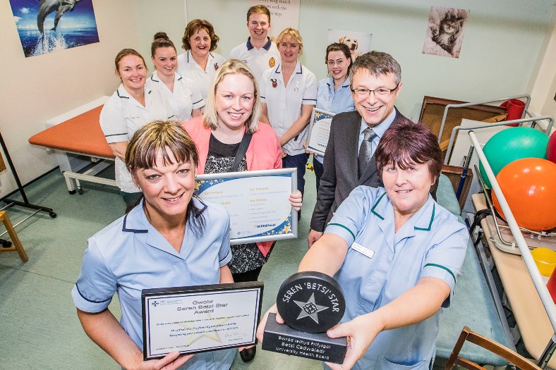 BCUHB Chief Executive Gary Doherty presents the first Seeren 'Betsi' Star award to the Stroke Early Supported Discharge Team at Ysbyty Glan Clwyd. Alaw Jones, Jamy Ashton and Shirley Heaven with the awrd and team members Ailsa Lucking, Julie Hirst, Mari Roberts, Lavinia Tilley, Maureen Bartley and Zach Spargo looking on.